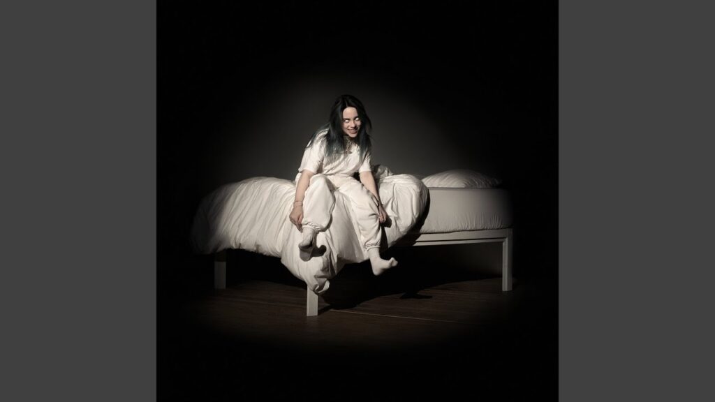 Billie Eilish sitting on the edge of a white bed in a dark, eerie room with glowing white eyes, wearing all white, in the haunting artwork for her album "When We All Fall Asleep, Where Do We Go?."